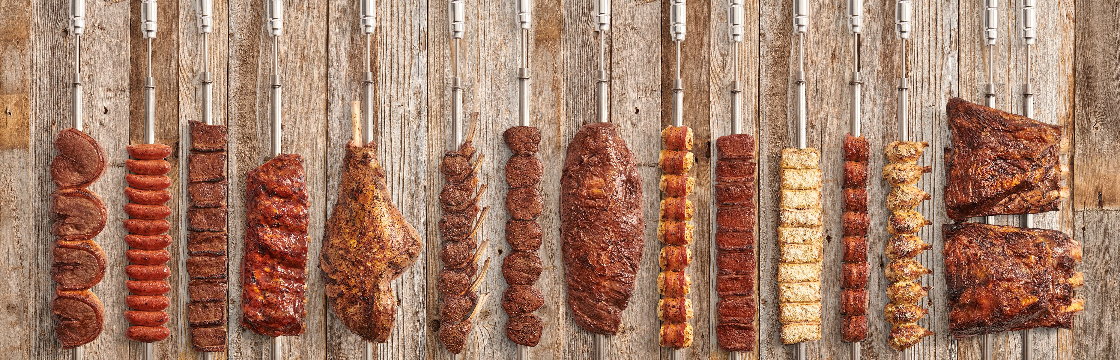 Diferentes carnes preparadas em espetos sobre fundo de madeira